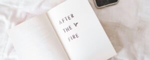 An open book on a bed reading 'AFTER THE FIRE,' symbolizing personal growth and starting over after crisis or challenges through The Holistic Life Coach Auckland.